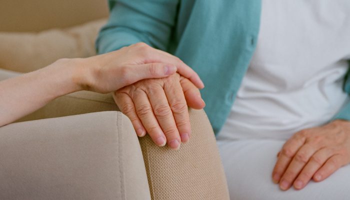 Caregiver cheers up senior lady patient touching hand while sits in armchairs in light room at long term care home closeup